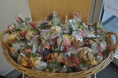 Ein Korb aus Weide gefüllt mit verschiedenen einzeln verpackten Süßigkeiten und Keksen, einige in Plastik verpackt mit dekorativen Bändern und Blättern, auf einem Tisch in der Nähe einer Glastür platziert.