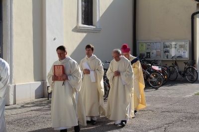 Vier Priester gehen gemeinsam auf einer Straße, halten Bücher und im Hintergrund sind Fahrräder geparkt.