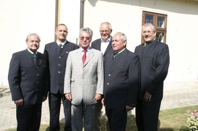 Sieben Männer in Anzügen und Krawatten stehen in einer Reihe vor einem Gebäude. Sie scheinen für ein Foto zu posieren.