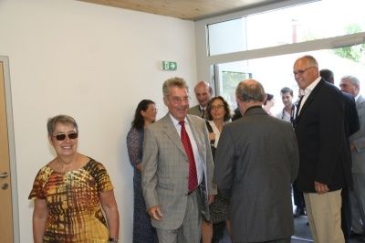 Eine Gruppe von Menschen, darunter mehrere Männer in Anzügen und Krawatten, stehen in einem Raum. Ein Mann trägt eine Brille und ein anderer eine Halskette.