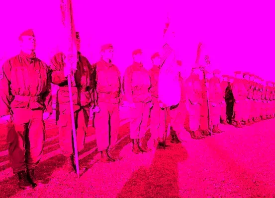 Eine Gruppe von Soldaten steht in einer Reihe und hält Fahnen, unter einem hellen rosa Himmel.