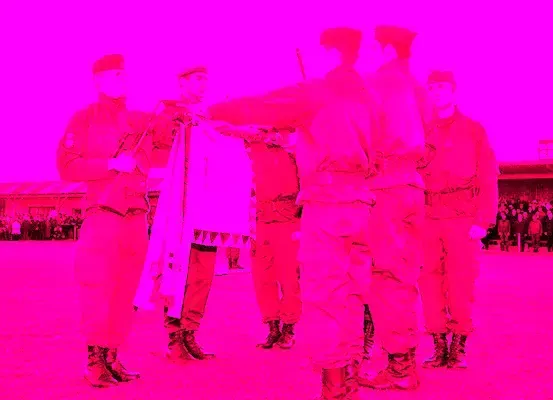 Eine Gruppe von Soldaten in roten Uniformen steht im Kreis und hält ein Banner hoch, mit einer Menge im Hintergrund.