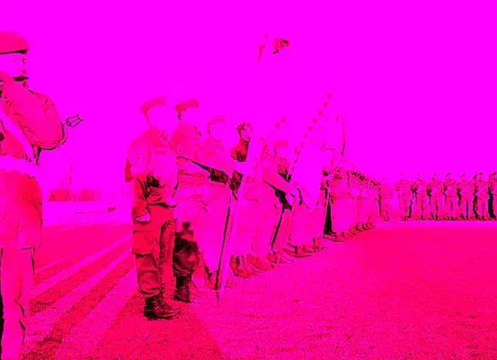 Eine Reihe von Soldaten steht in Formation auf einer Straße unter einem leuchtend rosa Himmel, ein Soldat in der Front bläst eine Trompete.