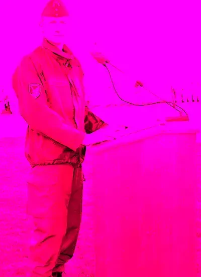 Ein Mann in einer roten Militäruniform steht an einem Podium mit einem Mikrofon vor ihm, wahrscheinlich hält er eine Rede.