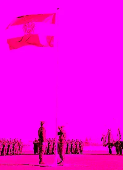 Eine rote Fahne mit Logo weht auf einem Pfahl. Zwei Soldaten stehen und scheinen die Flagge zu salutieren. Viele Soldaten stehen in Reihen. Der Hintergrund ist pink.