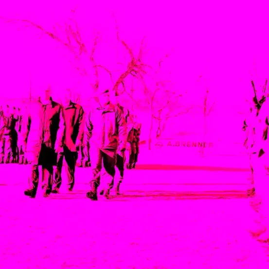 Eine Gruppe von Menschen in roter Kleidung geht auf einer rosa getönten Straße mit Bäumen und einem Gebäude im Hintergrund.