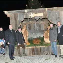 Eine Gruppe von Männern und ein Kind in einem Kinderwagen stehen bei Nacht vor einer Krippe.