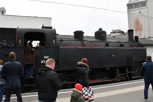 Menschen stehen auf einem Bahnsteig in der Nähe eines Zuges, einer steigt durch die offene Tür ein. Der Zug hat '4' auf beiden Seiten, und '088 93' ist darauf gemalt.