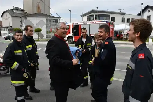 Eine Gruppe von Feuerwehrleuten steht mit einem Mann im Anzug draußen. Sie stehen vor einem Feuerwehrwagen.