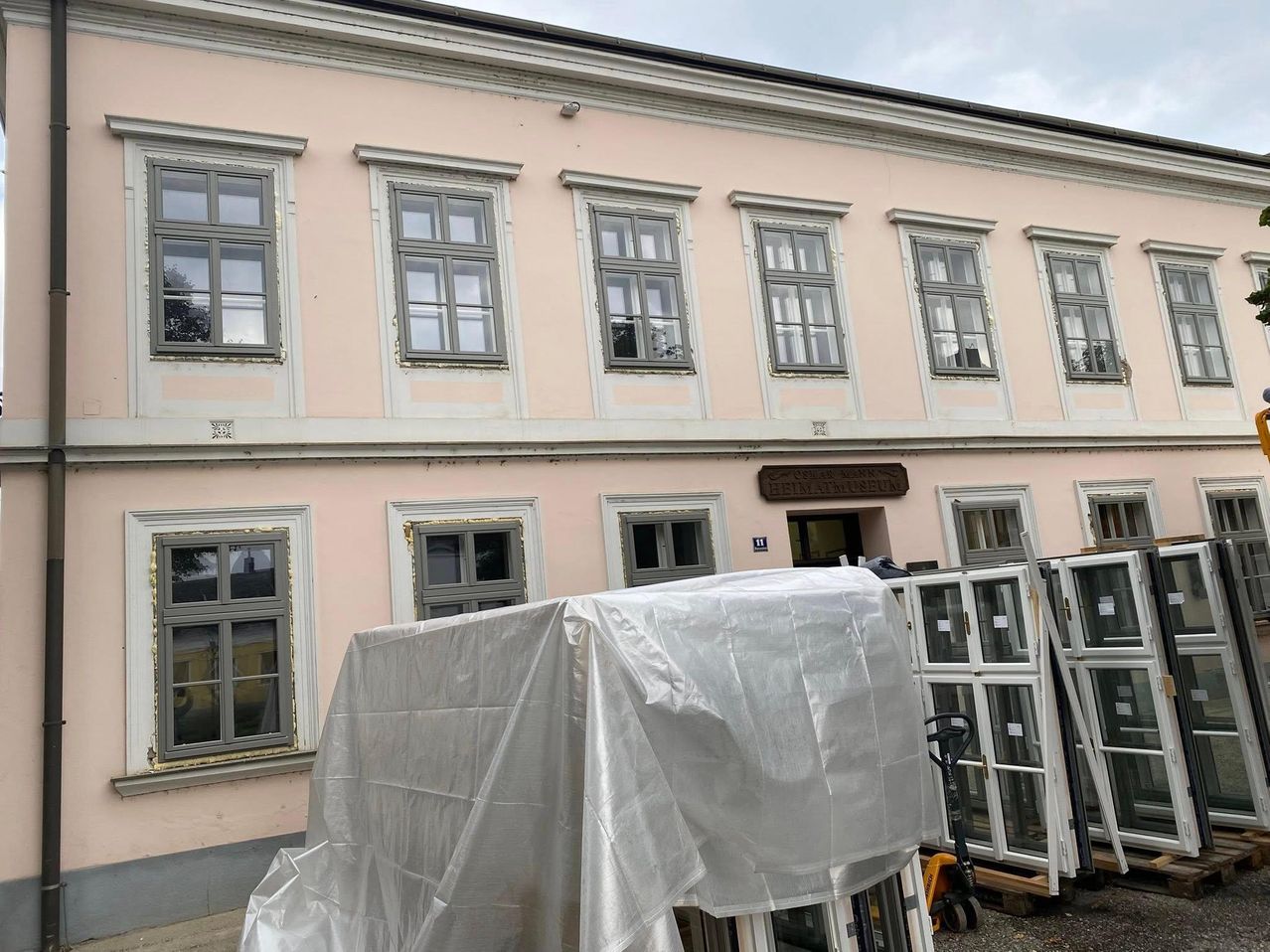 Ein rosafarbenes Gebäude mit mehreren Glasfenstern, einem abgedeckten Gegenstand davor und Lagerung an der Seite.