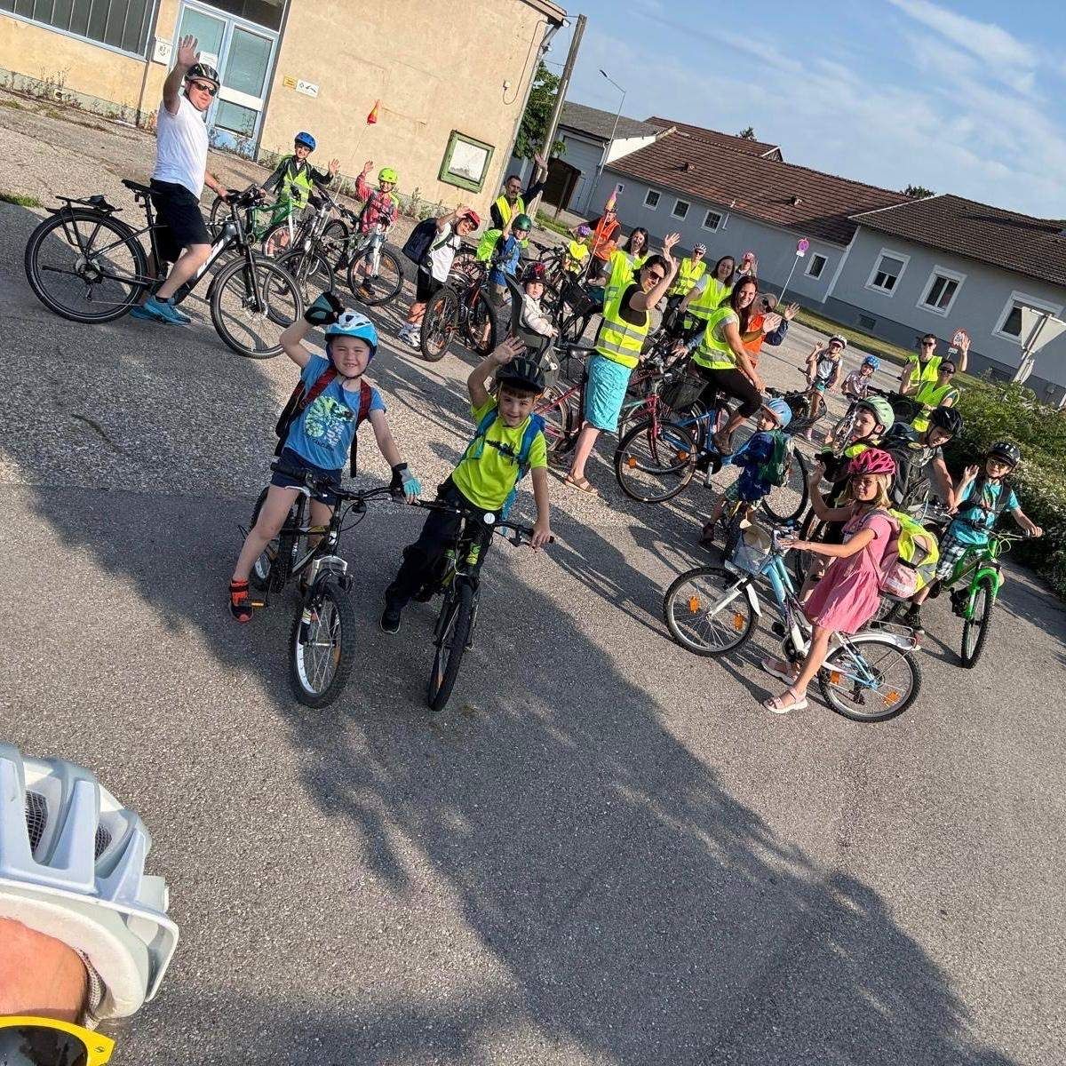 Eine Gruppe von Kindern, zusammen mit Erwachsenen, fährt auf einem gepflasterten Weg mit ihren Fahrrädern. Die Kinder tragen Sicherheitswesten.