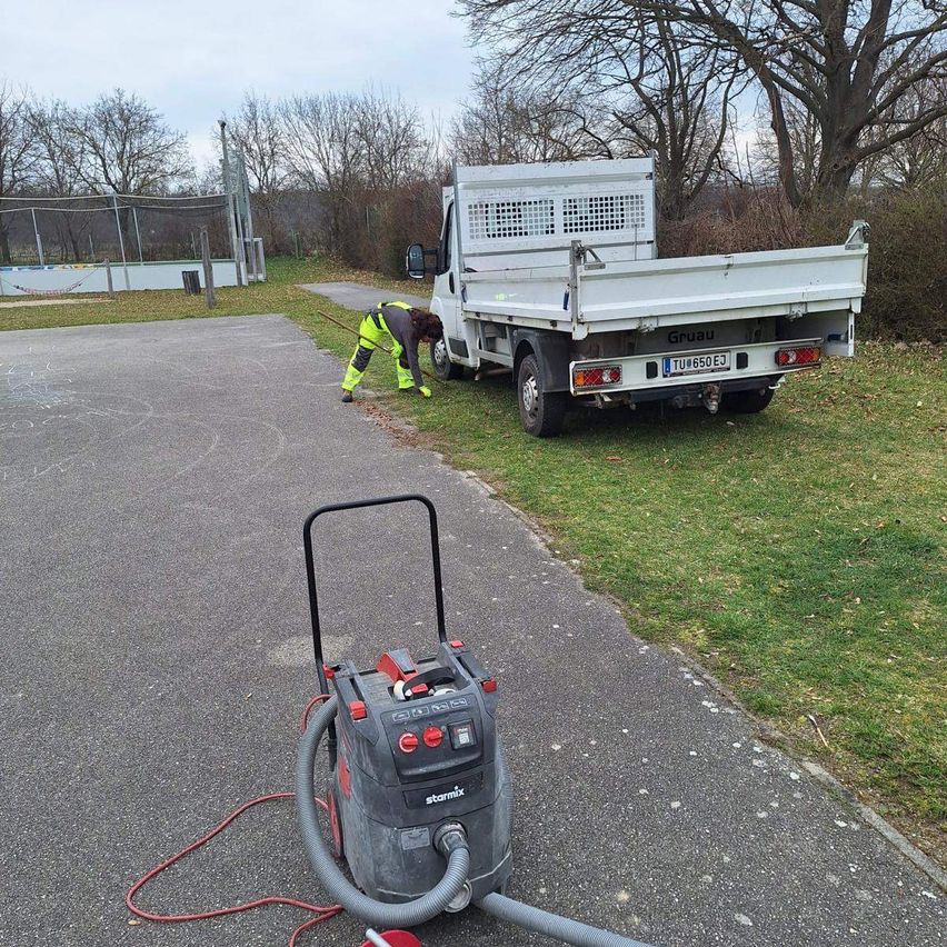 Ein Arbeiter reinigt Gras in der Nähe eines geparkten Trucks mit dem Kennzeichen TU 650 EJ. Der Truck steht auf einem Grasfeld, an dem ein roter Schlauch an einer Starmix-Maschine angeschlossen ist.