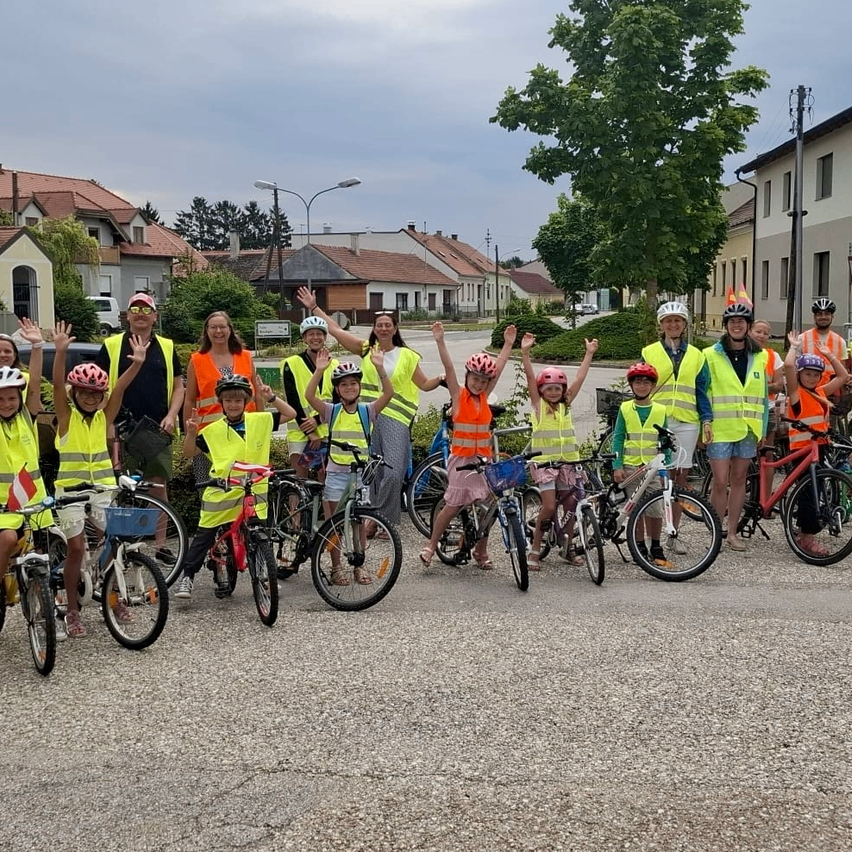 Eine Gruppe von Kindern und Erwachsenen in Sicherheitswesten und Helmen steht mit ihren Fahrrädern auf einer Schotterstraße.