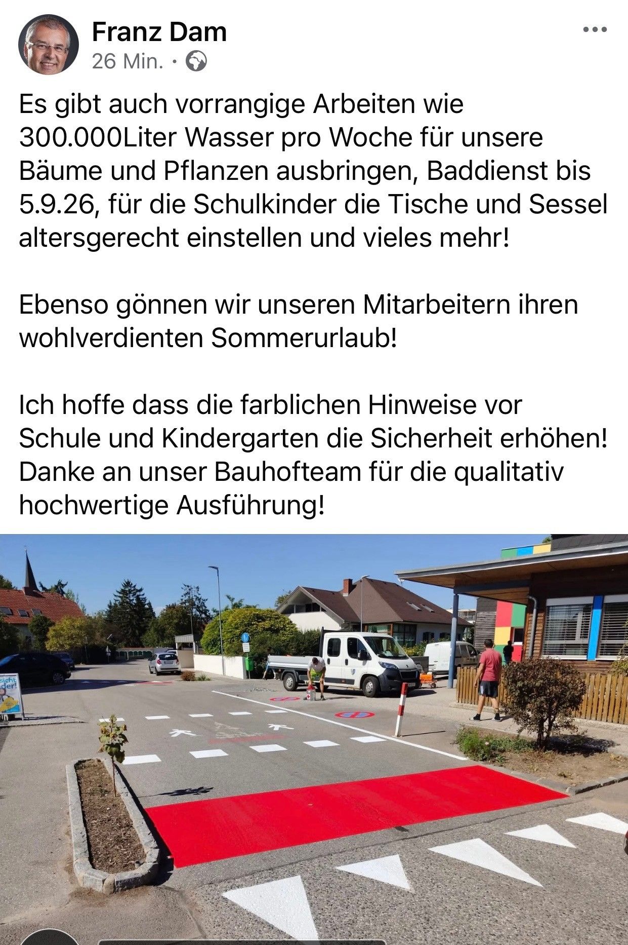 Eine Straßenszene mit einem geparkten weißen Lieferwagen, einem gehenden Menschen und einem Gebäude mit bunten Wänden. Bäume und Pflanzen im Hintergrund, ein Schild ist sichtbar.