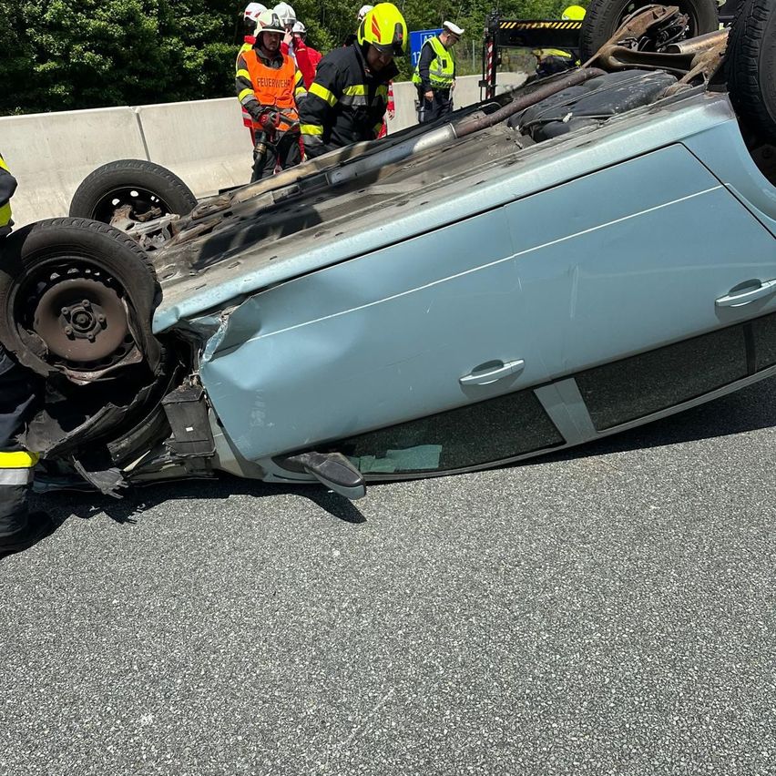 Einsatzkräfte kümmern sich um ein beschädigtes Auto, das auf der Straße auf dem Dach liegt.