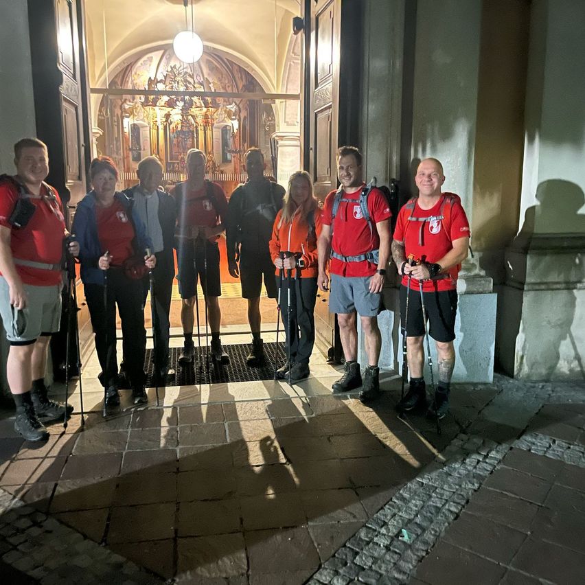 Eine Gruppe von Wanderern in roten T-Shirts und schwarzen Shorts posiert nachts vor einem Kircheneingang.