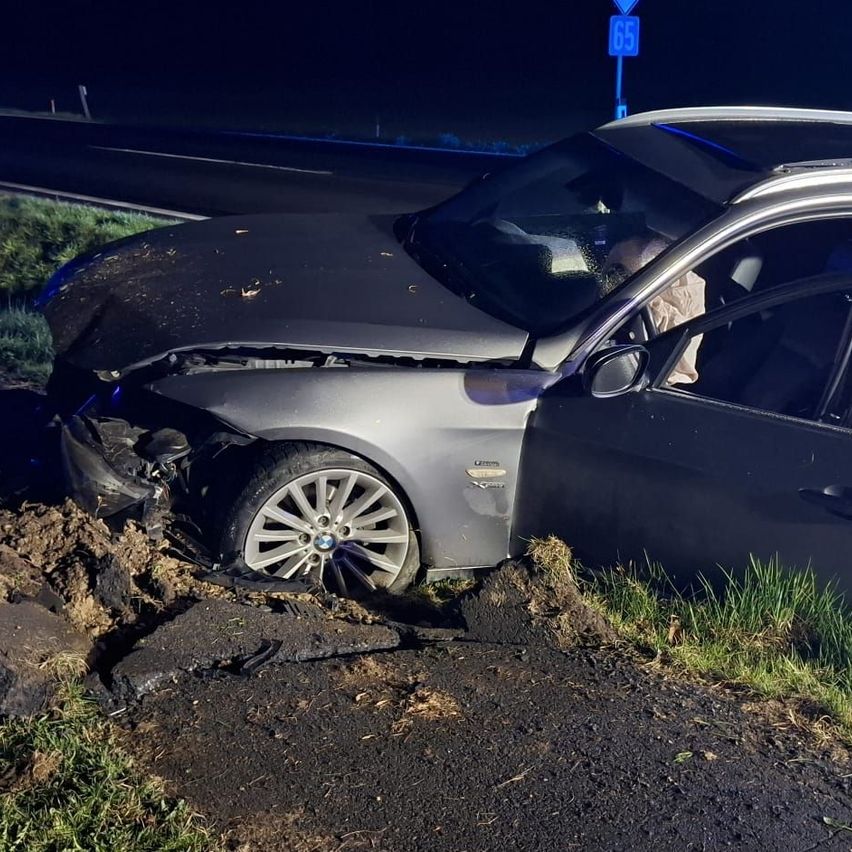 Ein beschädigtes BMW-Fahrzeug steht auf der Seite einer Straße, der Vorderteil stark beschädigt, in der Nähe eines Autobahnschilds für 65.