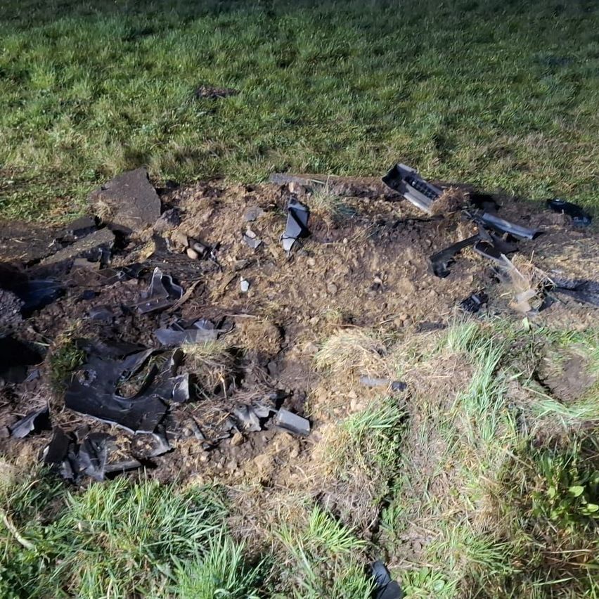 Ein verbrannter Bereich mit schwarzen verbrannten Trümmern und Überresten eines Geräts, das auf dem Boden in einem Grasfeld verstreut ist.