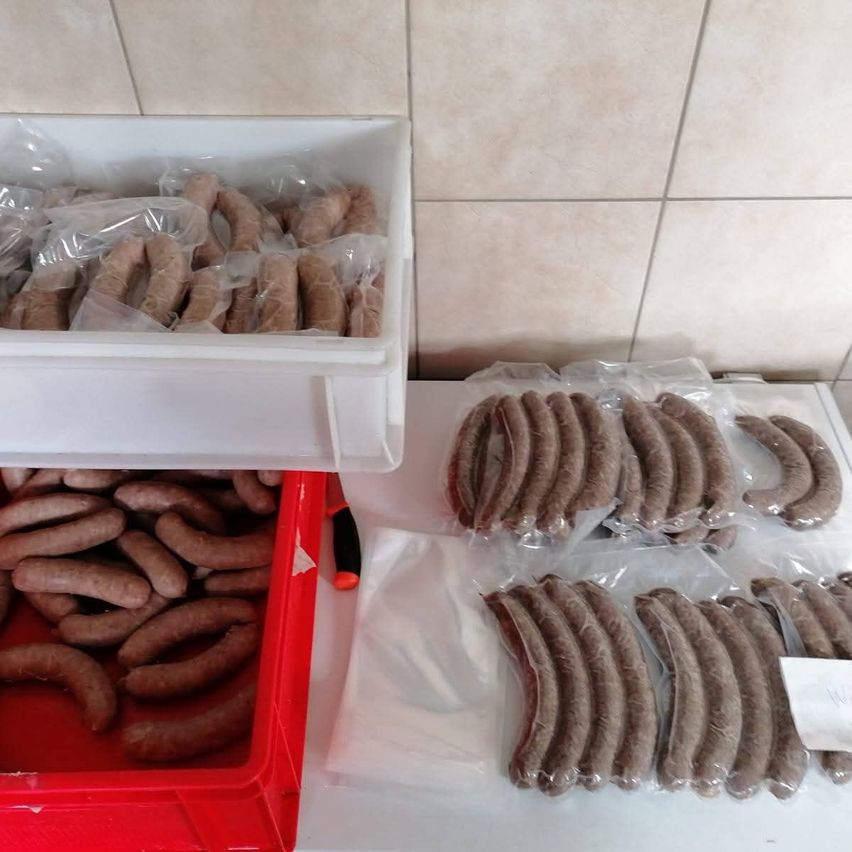 Zwei Behälter mit Würstchen in Plastiktüten auf einer weißen Oberfläche, ein Behälter ist rot und der andere weiß. Ein Messer ragt aus dem roten Behälter heraus. Der Hintergrund ist gefliest.