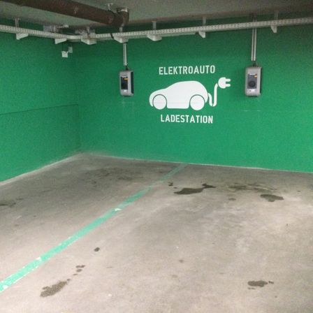Ein leerer Parkplatz mit grünen Wänden, zwei Elektroauto-Ladestationen und einigen Wasserflecken auf dem Boden.