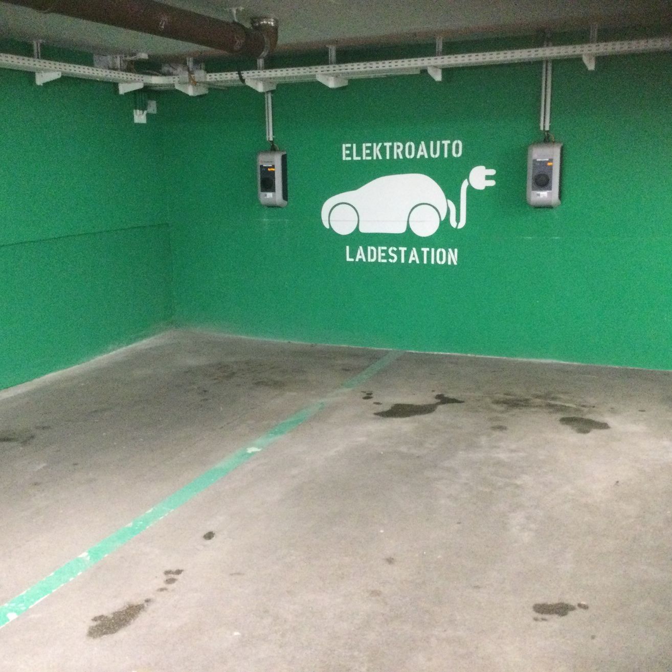 Ein leerer Parkplatz mit grünen Wänden, zwei Elektroauto-Ladestationen und einigen Wasserflecken auf dem Boden.
