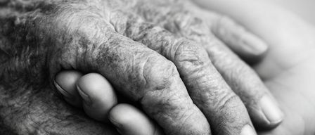 Ein schwarz-weißes Bild zeigt zwei ältere Hände, die sich gegenseitig halten. Der obere Text lautet 'LETZTE-HILFE-KURS AM ENDE WISSEN, WIE ES GEHT'. Unten an den Händen befindet sich ein orangefarbener Hintergrund mit weißem Text. Der untere Teil des Bildes zeigt ein Logo und den Text 'Wir sind, wo Sie sind.'