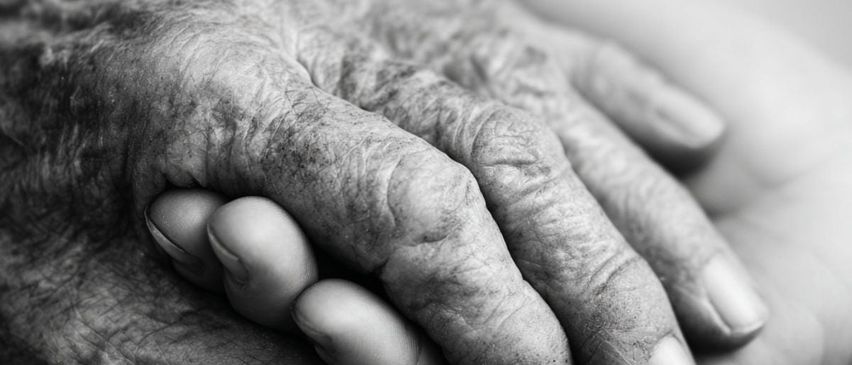 Ein schwarz-weißes Bild zeigt zwei ältere Hände, die sich gegenseitig halten. Der obere Text lautet 'LETZTE-HILFE-KURS AM ENDE WISSEN, WIE ES GEHT'. Unten an den Händen befindet sich ein orangefarbener Hintergrund mit weißem Text. Der untere Teil des Bildes zeigt ein Logo und den Text 'Wir sind, wo Sie sind.'