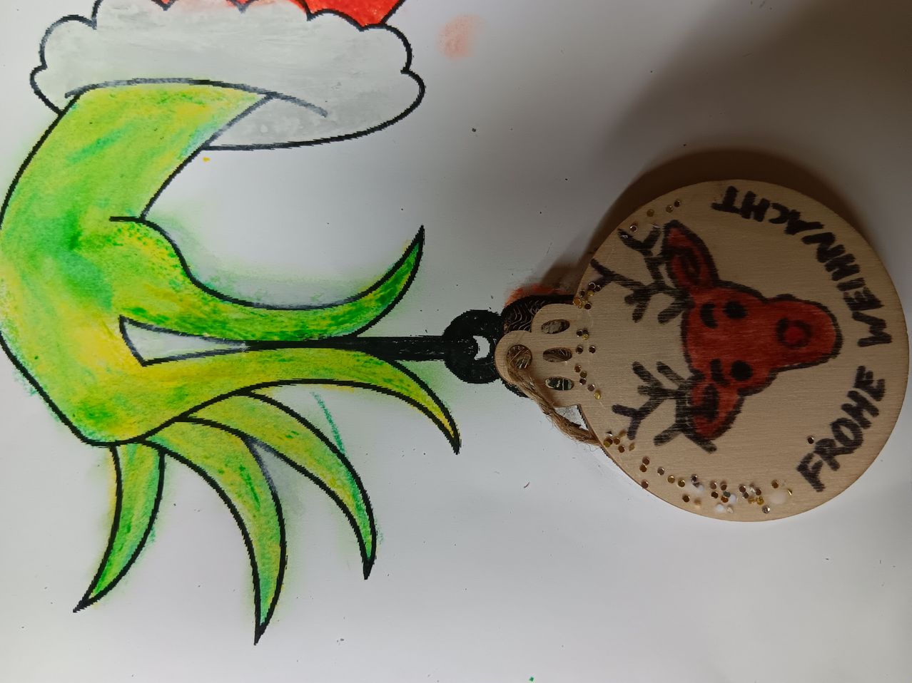 Ein Nahaufnahme einer Weihnachtsdekoration mit einem Holzornament, das einen roten Rentier zeigt. Das Ornament hat eine schwarze Schnur befestigt und steht auf einem weißen Hintergrund.