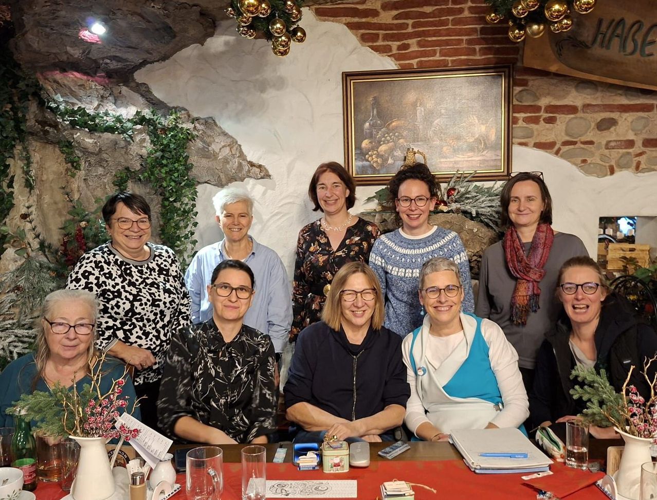 Eine Gruppe von Frauen lächelt für ein Foto in einem Raum mit einer Ziegelwand und Dekorationen. Sie sitzen um einen Tisch mit verschiedenen Gegenständen.