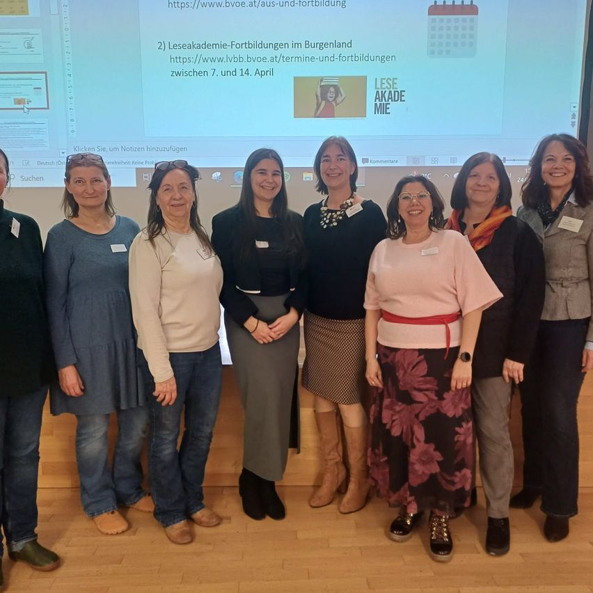 Eine Gruppe von Frauen posiert vor einer Projektionsleinwand, die einen Kalender und Veranstaltungsinformationen anzeigt.