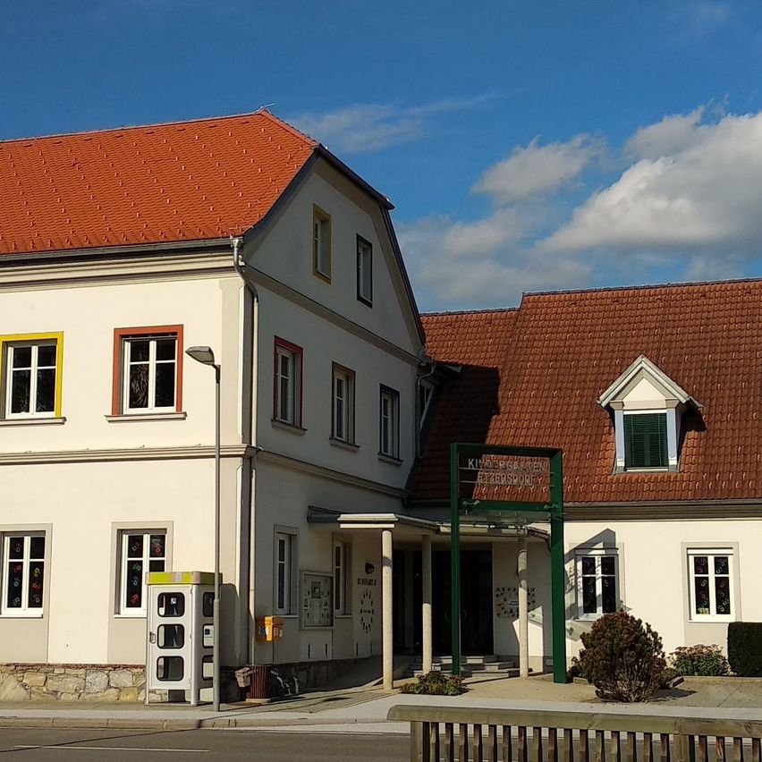 Ein weißes Gebäude mit roten Dächern und gelben Fensterumrandungen. Es befindet sich an einer Straße mit einem Holzzaun davor.