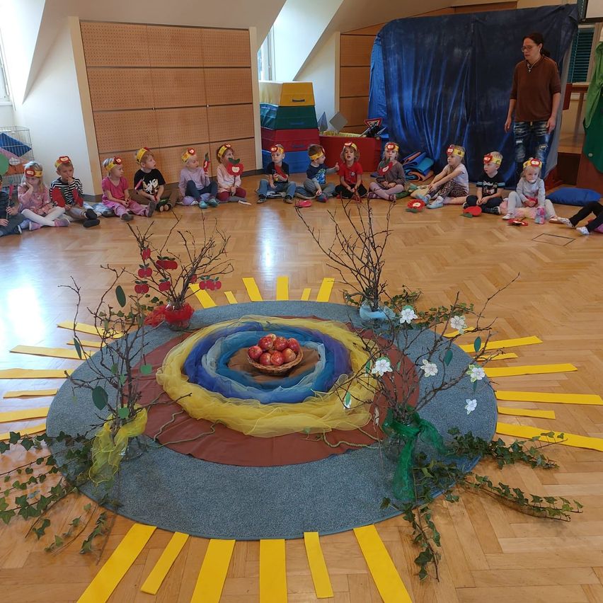 Eine Gruppe von Kindern im Kreis um einen dekorierten Tisch mit einer Frau vor ihnen.