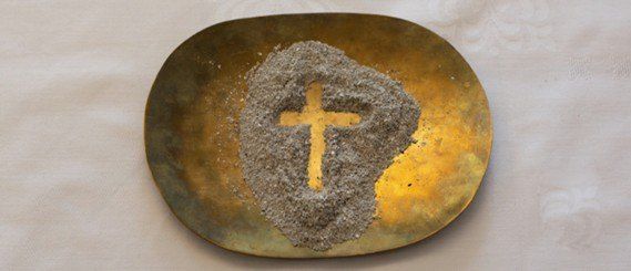 Eine goldene Platte zeigt ein Kreuz aus kleinen Steinen oder Kieseln, die auf einem weißen Tuch liegen.