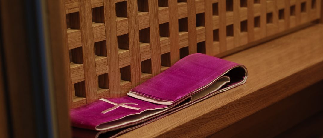 Ein rosafarbener Samtstola liegt gefaltet auf einer Holzbank. Die Bank hat ein Gittermuster.