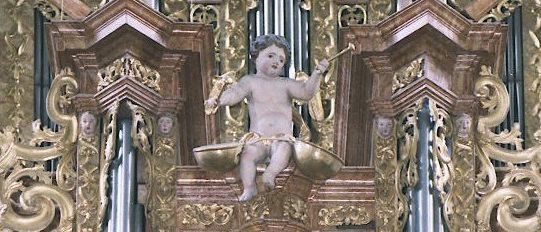 Eine kunstvolle Orgel mit einer Cherub-Statue, die auf einer goldenen Waage sitzt, umgeben von kunstvollen Golddesigns und Cherub-Köpfen.