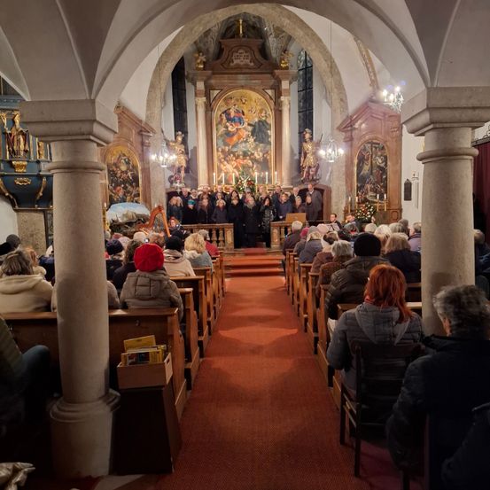 Ein Chor tritt in einer Kirche auf, die mit Menschen gefüllt ist. Die Kirche hat einen Altar mit Kerzen und Gemälden, und eine Harfe befindet sich auf der linken Seite.