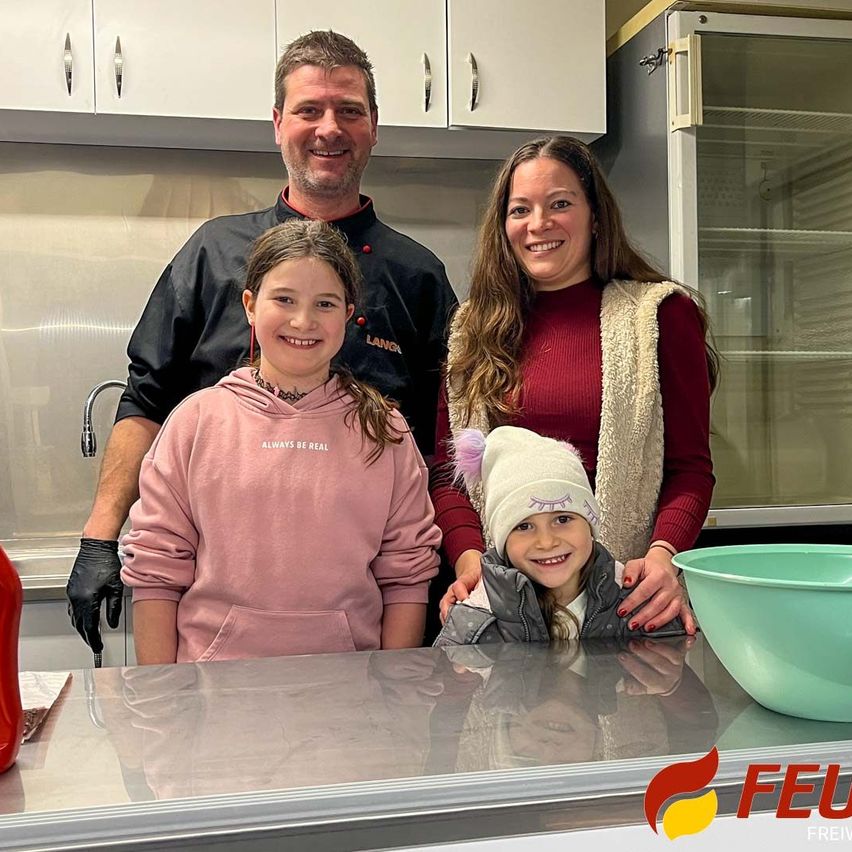 Eine Familie mit drei Personen in einer Küche, lächelt für ein Foto. Ein Mann und eine Frau stehen hinter einem jungen Mädchen und einem jungen Kind. Sie befinden sich in der Nähe einer Arbeitsplatte mit einer Schüssel.