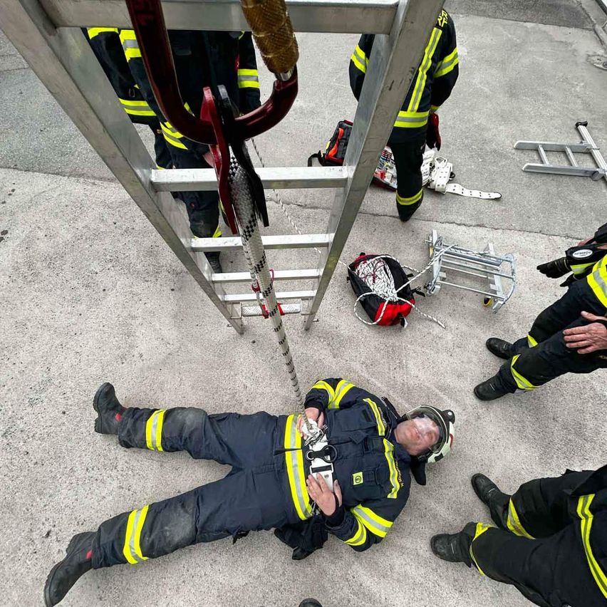 Feuerwehrleute in voller Montur liegen auf dem Boden, um sie herum Ausrüstung und Leitern. Einer trägt einen Helm und scheint zu schlafen.