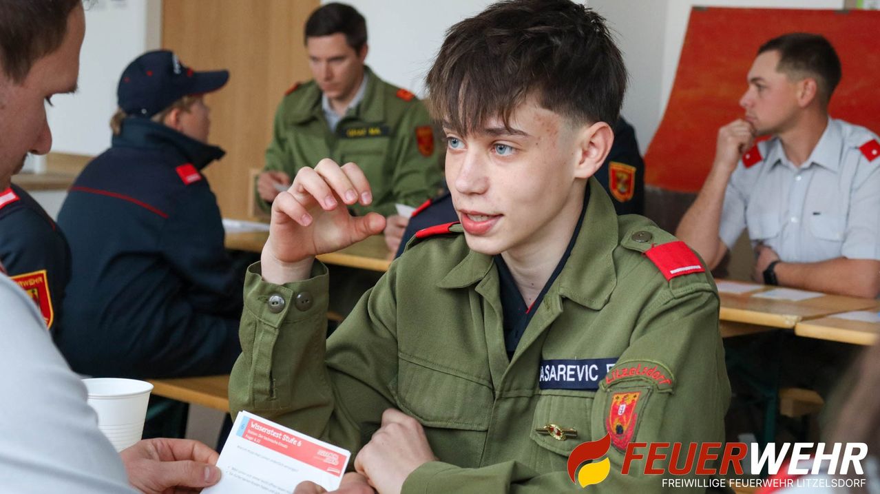 Ein junger Mann in Uniform hält ein Blatt Papier und hört aufmerksam zu, möglicherweise in einer Schulung, mit anderen in Uniform hinter ihm.