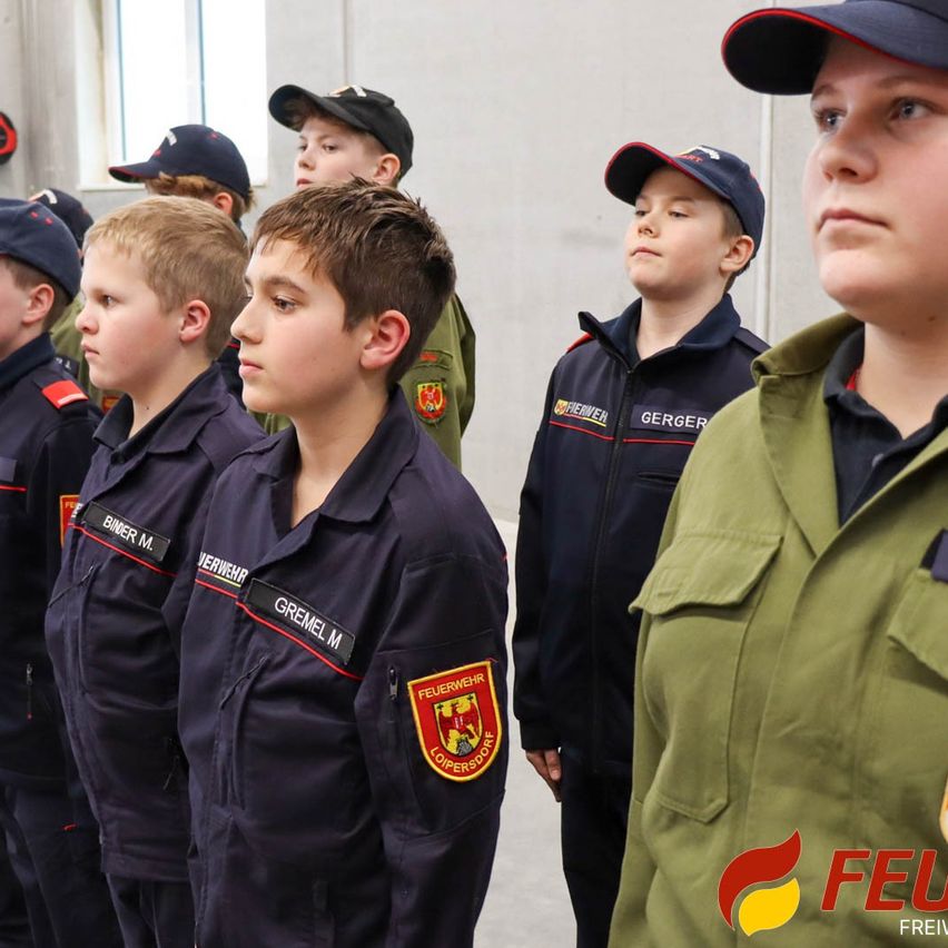 Mehrere Jungen in Uniform, möglicherweise Feuerwehrleute, stehen in einer Reihe. Sie tragen Mützen und Uniformen. Ein Logo auf ihren Uniformen lautet 'FEUERWEHR LOPERSDORF'.