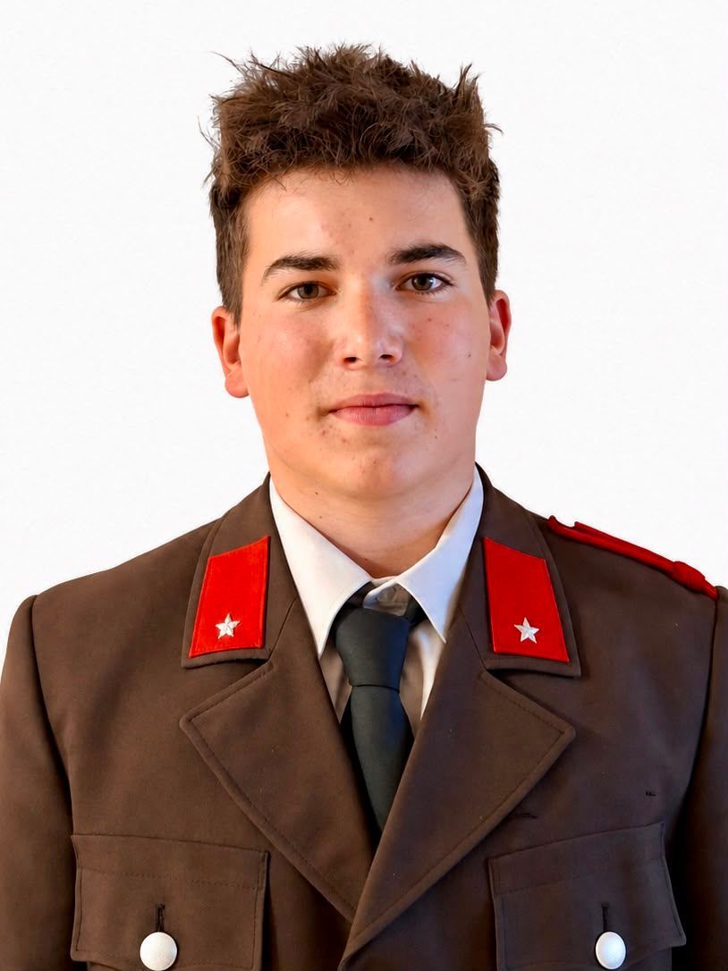 A young man in a military uniform with red shoulder patches and a star insignia, standing against a plain white background.