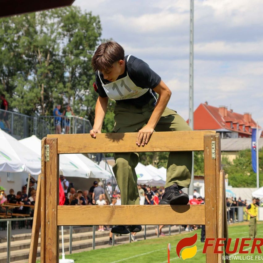 Ein junger Junge, der ein schwarzes und weißes Shirt mit der Nummer 17 trägt, springt über eine Holzhürde bei einer Veranstaltung im Freien.