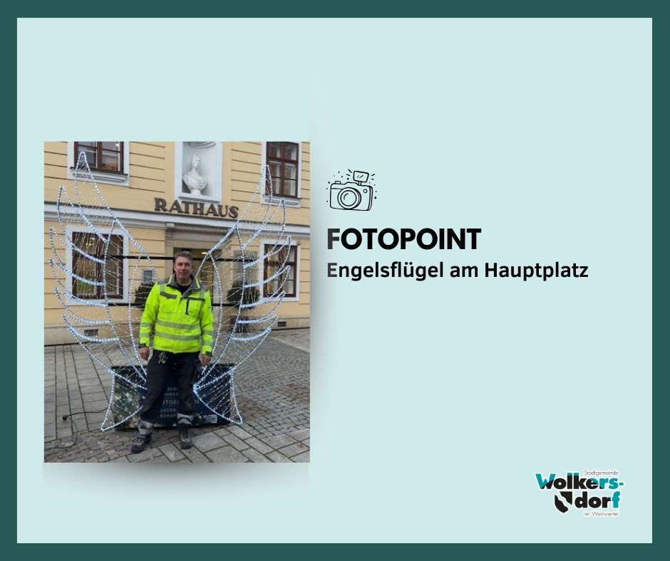 Ein Mann in einer gelben Jacke steht vor dem Rathausgebäude mit Engelsflügeln auf dem Hauptplatz.