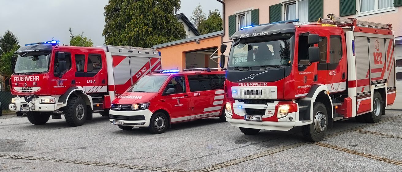 Zwei Einsatzfahrzeuge sind am Straßenrand geparkt, möglicherweise im Einsatz. Das Fahrzeug auf der linken Seite ist ein roter Van und das auf der rechten Seite ein großer Feuerwehrwagen.