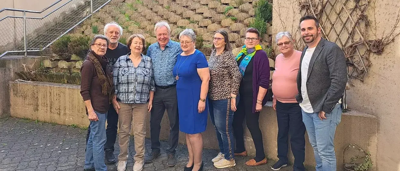 Eine Gruppe von Menschen posiert für ein Foto vor einem Gebäude mit einer Treppe und einem Zaun.