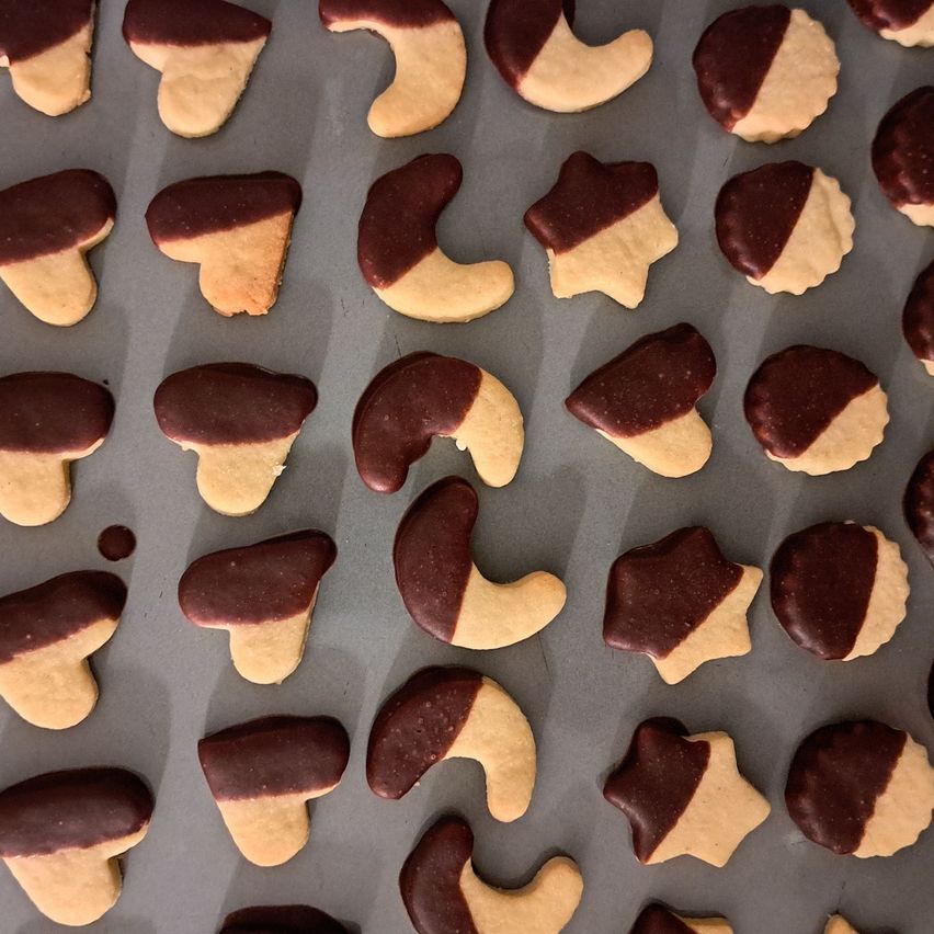 Ein Blech mit verschiedenen Keksen mit Schokoladenglasur, die in verschiedenen Formen wie Sternen, Halbmonden und Herzen angeordnet sind, auf einem Backblech platziert.