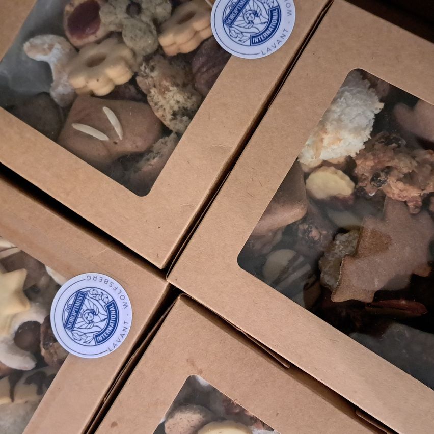 Mehrere braune Kartons mit verschiedenen Keksen gefüllt, darunter Schokoladenkekse, sternförmige und nussgefüllte Sorten, mit einem blauen Aufkleber, der 'International Von' besagt.