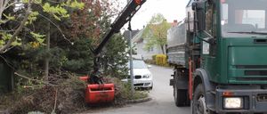 Ein Mann in einem grünen Jackett bedient einen Kran auf einem grünen Lastwagen und entfernt Äste von einem Baum in der Nähe einer Straße.