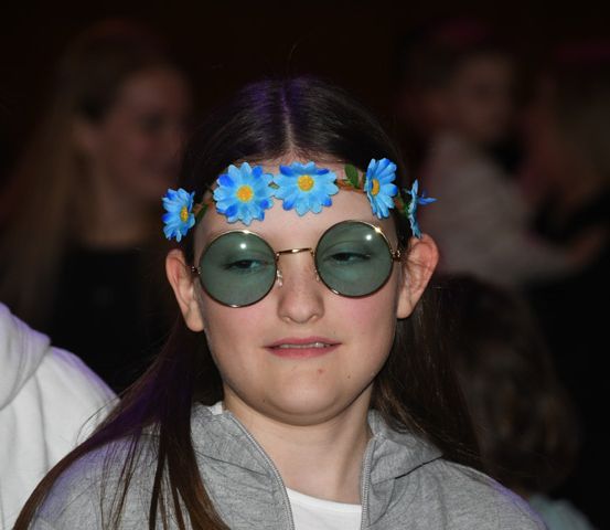 Ein Mädchen mit langen Haaren, das eine Blumenhaarspange und eine Sonnenbrille trägt, posiert für ein Foto.