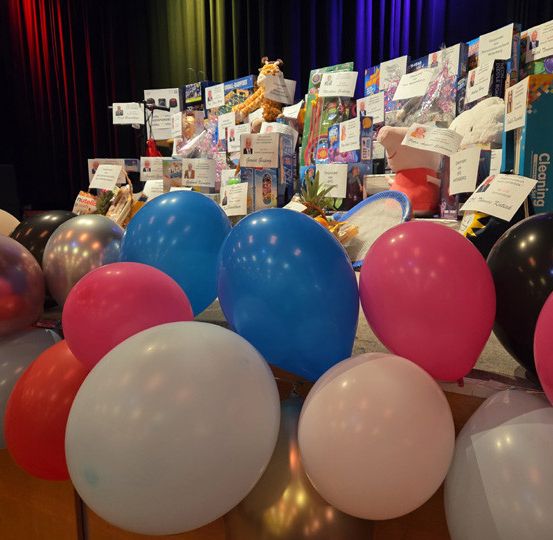 Eine Bühne mit einer Sammlung von Spielzeug und Ballons, darunter ein blauer und ein roter, vor einer Kulisse mit Karten angeordnet.